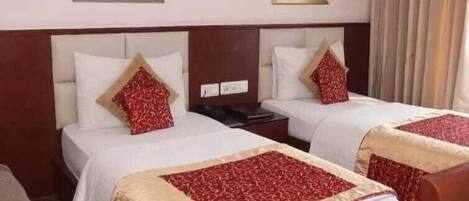 A hotel room with two beds, each with white linens and red patterned pillows. There are two paintings on the wall above the beds.