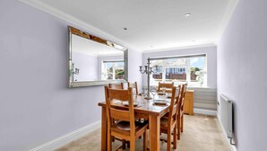Une salle à manger avec un grand miroir, des chaises en bois, une table dressée pour quatre personnes et une vue sur l’extérieur par une fenêtre.