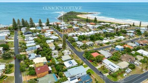 An aerial view of Cusack's Cottage, featuring a coastal setting with houses arranged in a grid pattern, surrounded by greenery and a beach.