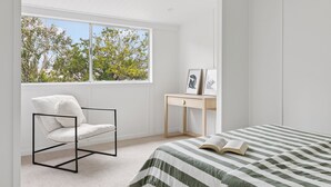 A bedroom with a bed, a chair, a desk, and a window with a view of trees.