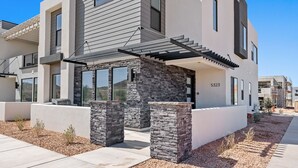 Une maison moderne à deux étages, dotée d’une façade en pierre, de grandes fenêtres et d’un espace extérieur couvert.