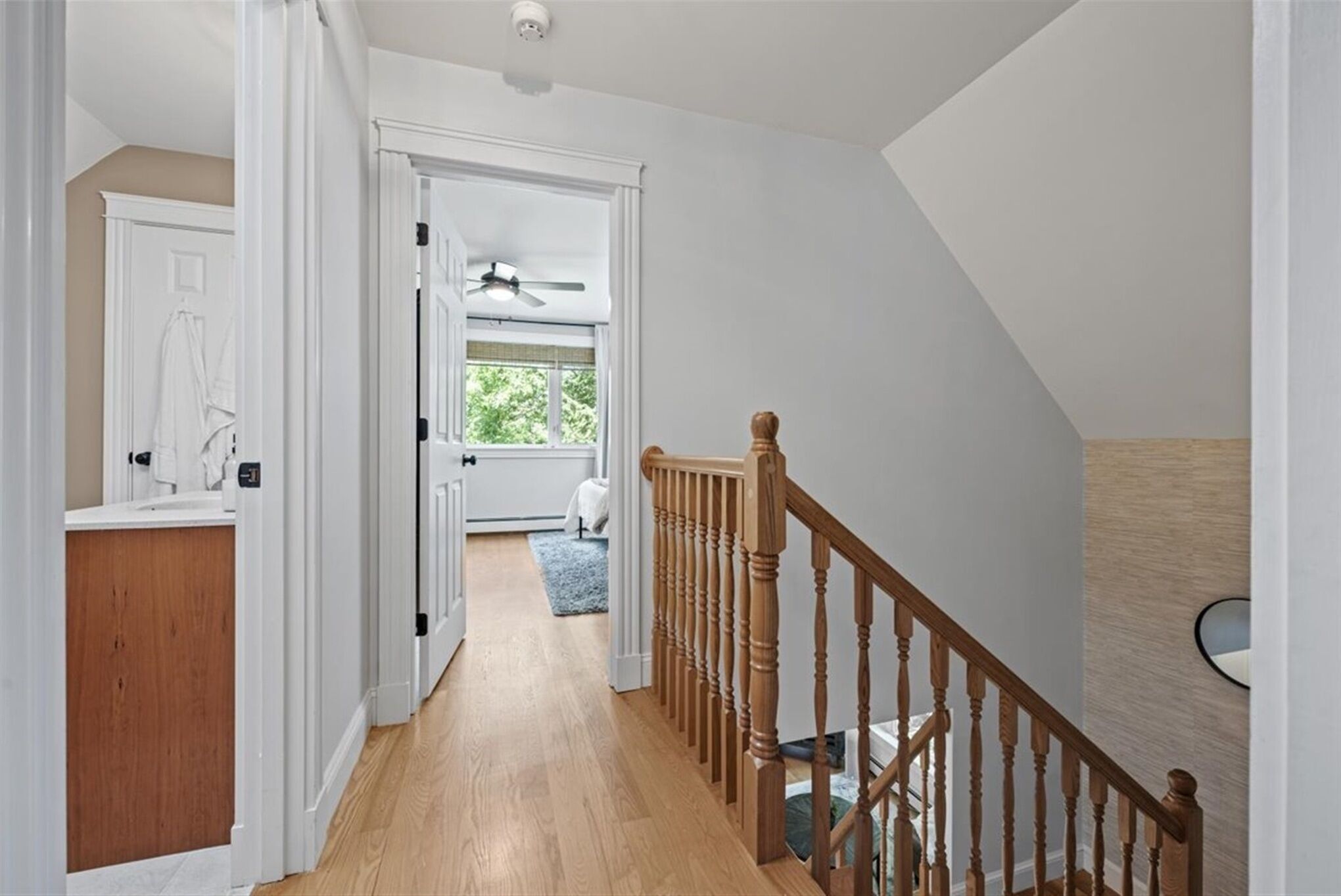 A hallway with wooden flooring, white walls, and a wooden staircase with a railing.