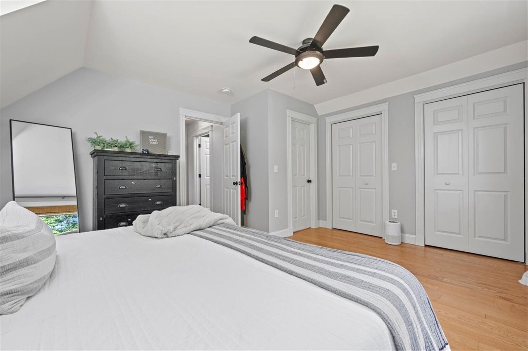 A bedroom with a bed, a dresser, a ceiling fan, and white doors.
