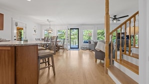 Une cuisine spacieuse avec un îlot central en bois, un coin repas avec des chaises et un escalier menant à un salon équipé d’un canapé et d’un téléviseur.