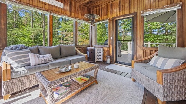 Une cabane en bois avec un porche couvert, deux canapés en osier, une table basse et une pancarte indiquant « Résidence au bord du lac ».