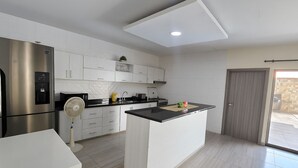 A modern kitchen with white cabinets, a stainless steel refrigerator, a built-in stove, and a small island with a black countertop. - Charming 3-bedroom chalet, with private pool, an with AC. (Malambo)