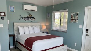 A bedroom with a bed, an air conditioner, a window with blinds, and a wall-mounted fish decoration. - Beachgate Condo Suites And Hotel 232 1 Bedroom Condo (Port Aransas)