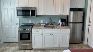 A compact kitchen with white cabinets, a stainless steel microwave, an oven, a sink, and a refrigerator. - Beachgate Condo Suites And Hotel 232 1 Bedroom Condo (Port Aransas)