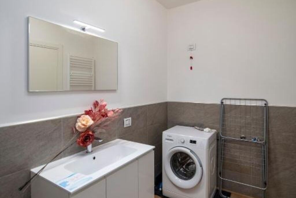 Un bagno compatto con lavandino bianco, uno specchio, una lavatrice e un porta asciugamani.