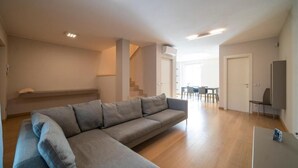A modern living room with a grey sectional sofa, wooden flooring, and recessed ceiling lights. - VILLA La No. 1 - Spacious & Modern (MONTICELLI BRUSATI)