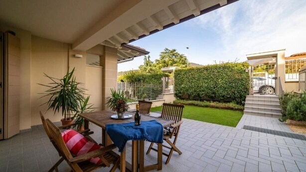 An outdoor patio with a wooden table and chairs, a potted plant, and a well-maintained lawn. - VILLA La No. 1 - Spacious & Modern (MONTICELLI BRUSATI)