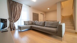 A modern living room with a grey sectional sofa, a flat-screen TV, and a staircase. - VILLA La No. 1 - Spacious & Modern (MONTICELLI BRUSATI)
