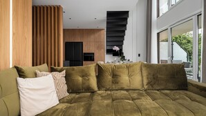 A modern living room with a sectional sofa, wooden paneling, and a view of the outdoors. - Apartamenty Sun & Snow Lake House (Serock)