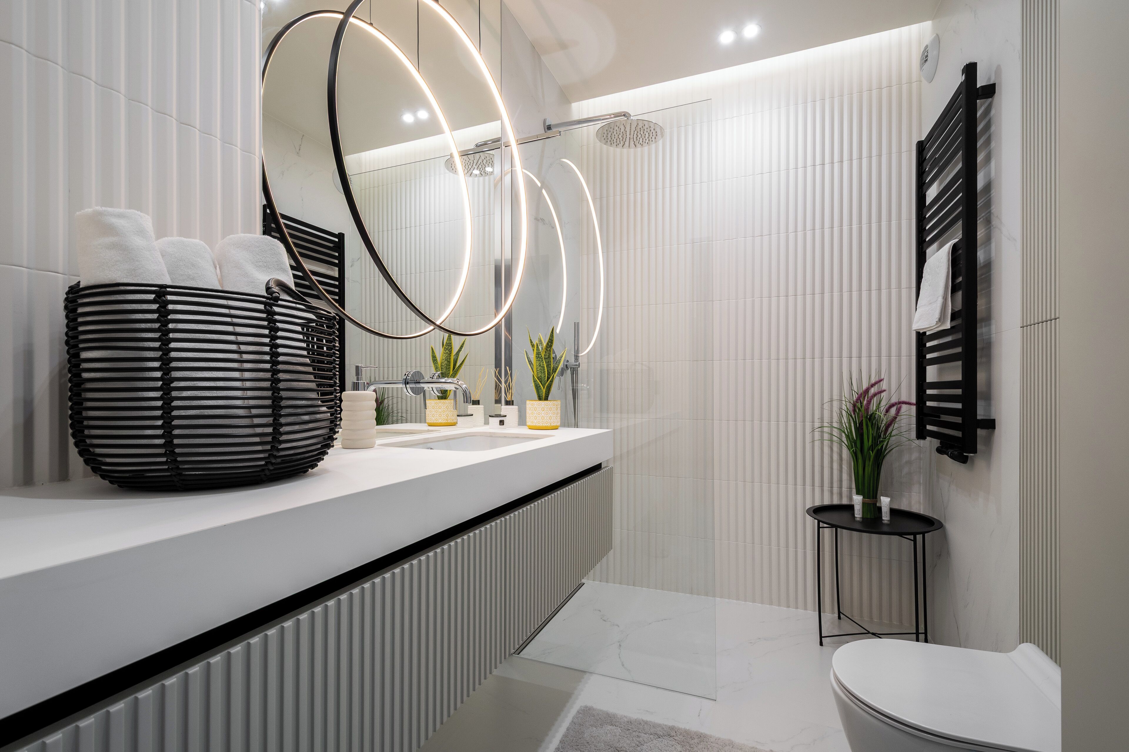 A modern bathroom with a white vanity, a black towel rack, and a small table with plants.