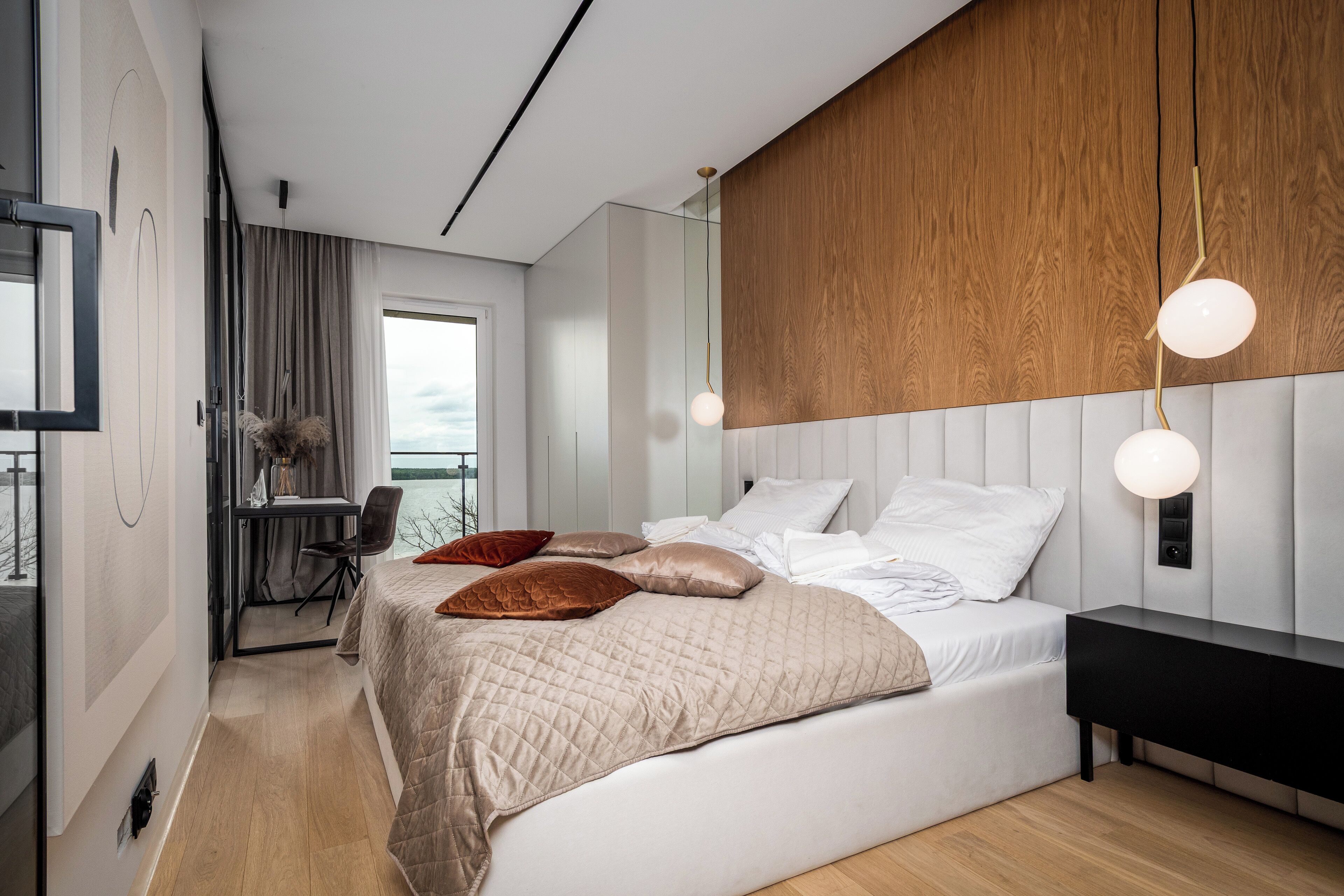 A modern bedroom with a large bed, a desk, and a view of the outdoors.