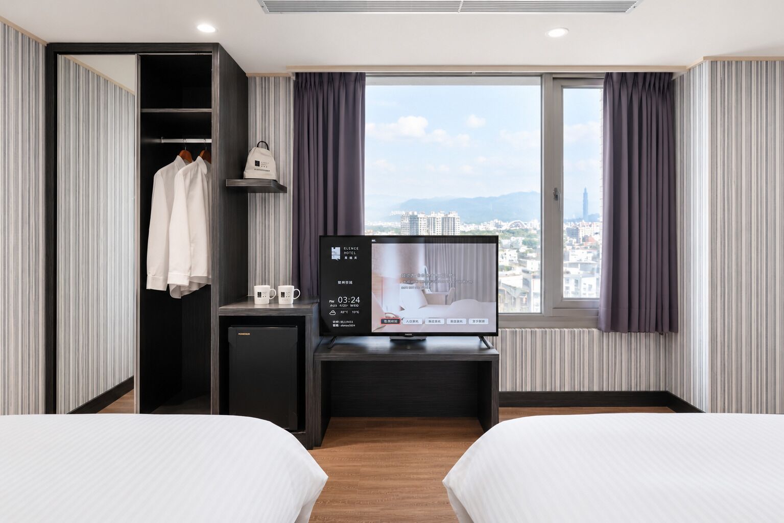 A hotel room with two beds, a desk with a TV, a mini-fridge, and a wardrobe.