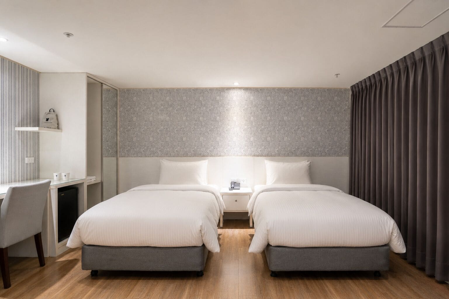 A hotel room with two beds, a desk, and a chair.