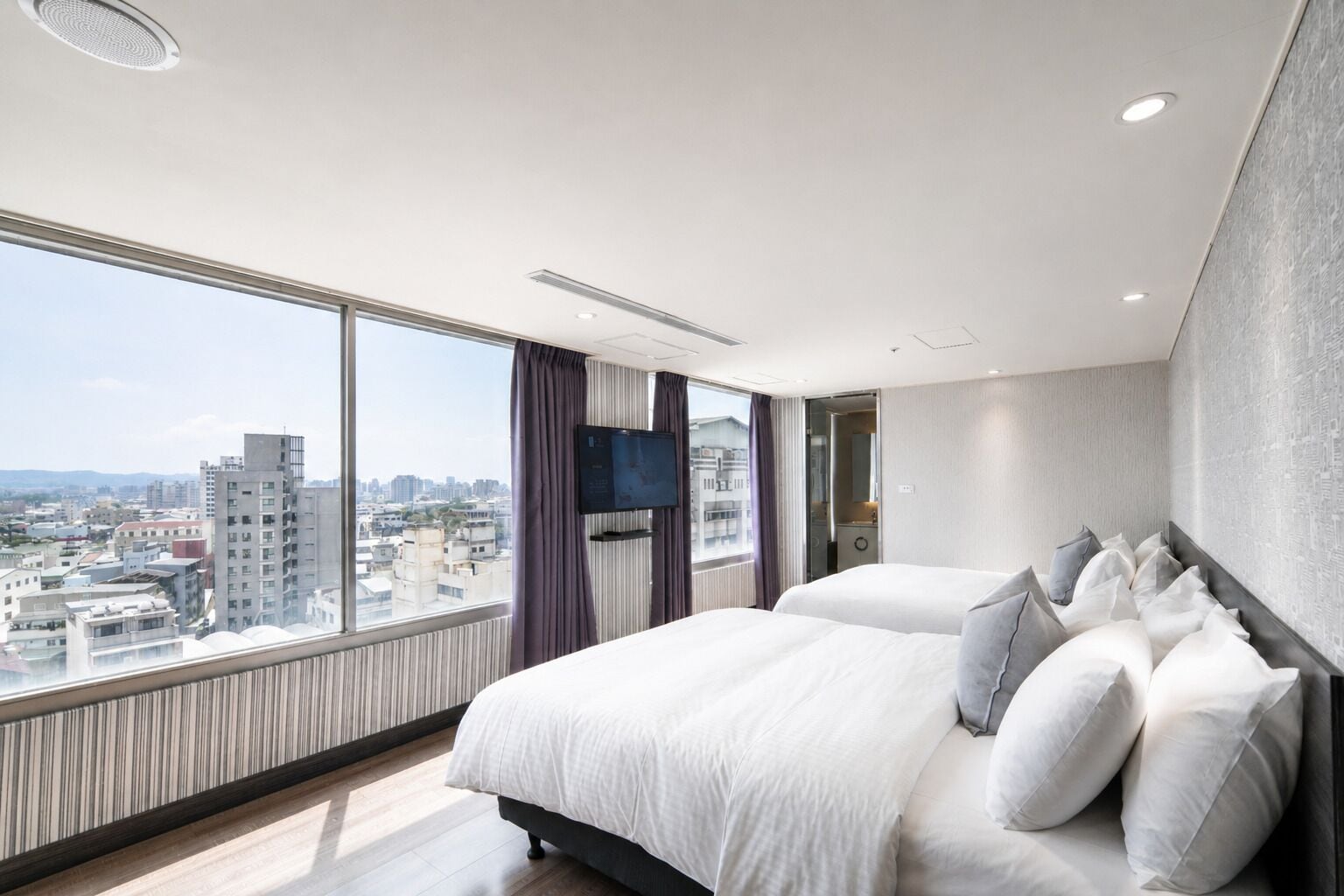 Een hotelkamer met een groot bed, een televisie en uitzicht op de stad.