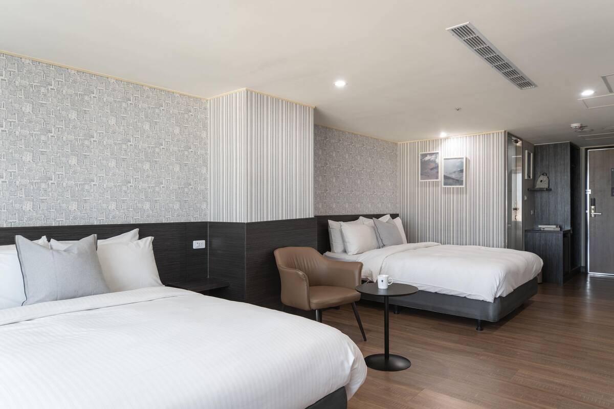 A hotel room with two beds, a chair, a small table, and a nightstand.
