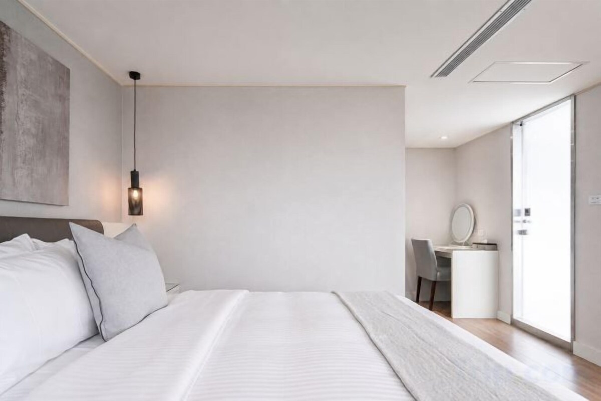 A modern bedroom with a large bed, bedside table, and a desk with a chair.