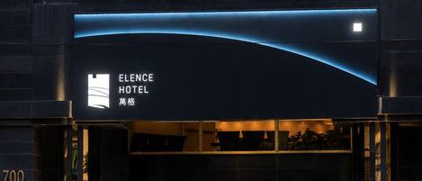 The exterior of the Elence Hotel with a modern design, featuring a prominent entrance and a digital signboard.