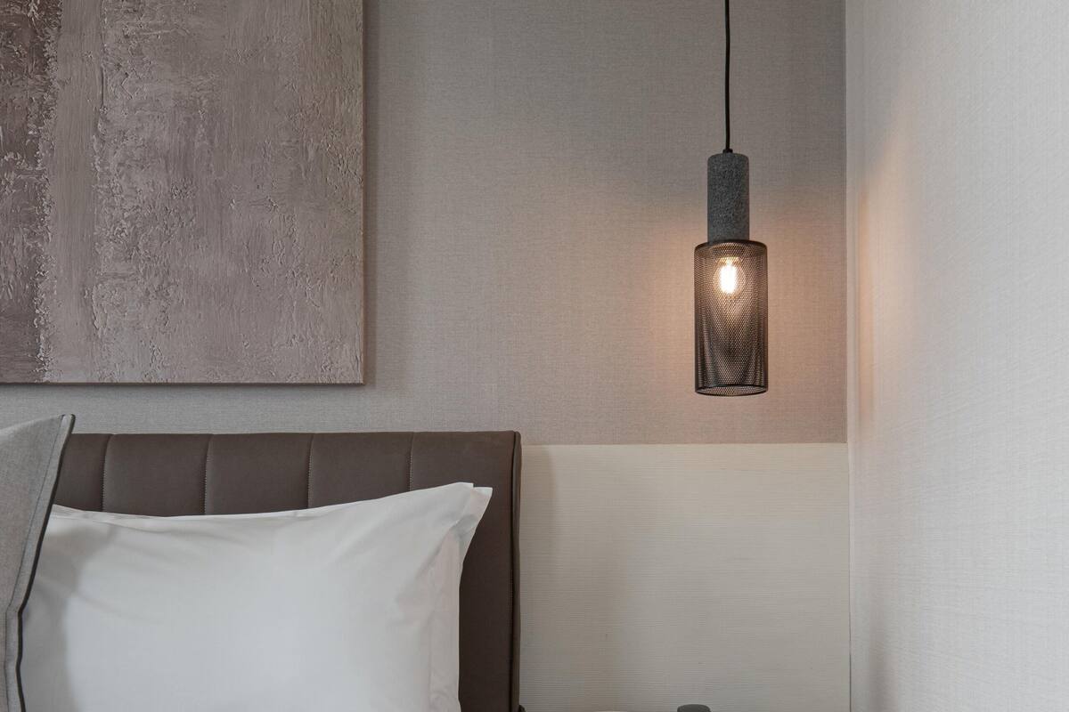 A neatly made bed with a headboard, a bedside table with a lamp, and a painting on the wall.