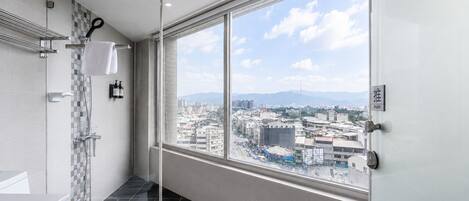A modern bathroom with a shower, toilet, and a large window offering a city view.