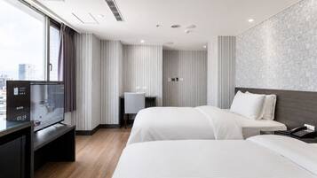 A hotel room with two beds, a desk, a TV, and a city view.