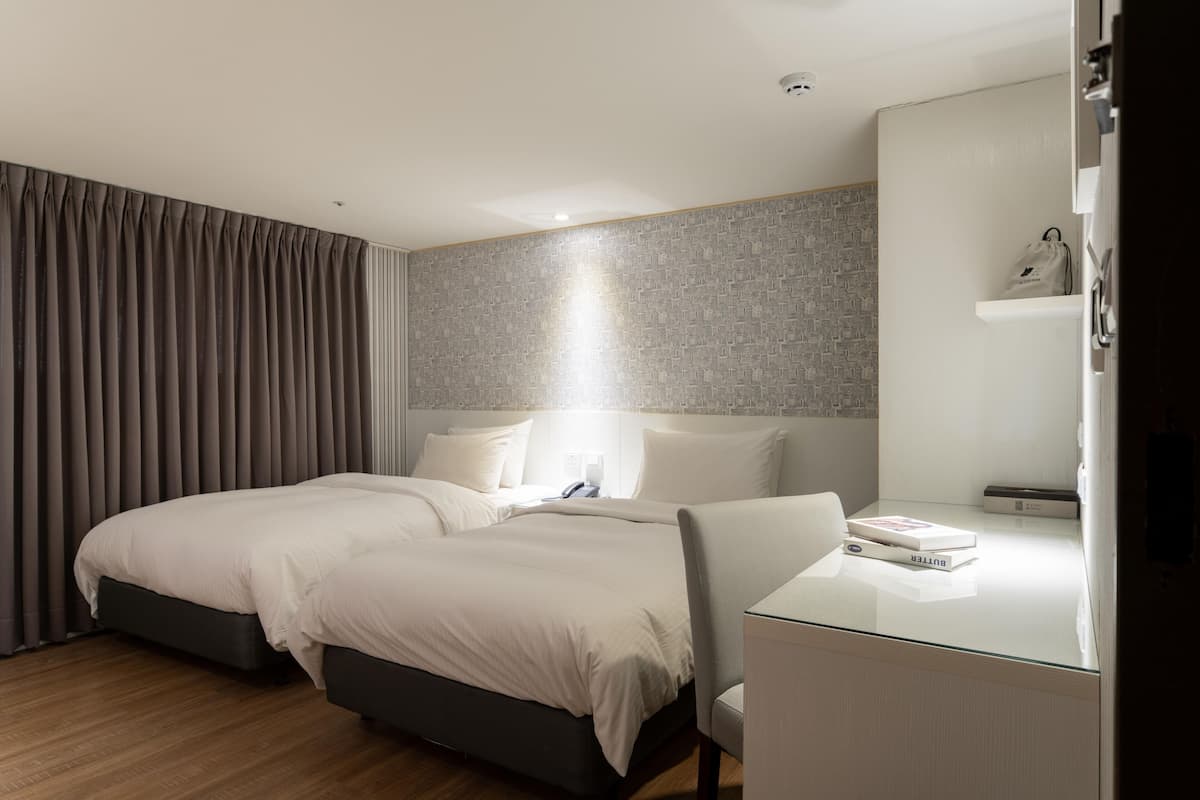 A modern hotel room with a large bed, a desk with a chair, and a nightstand.