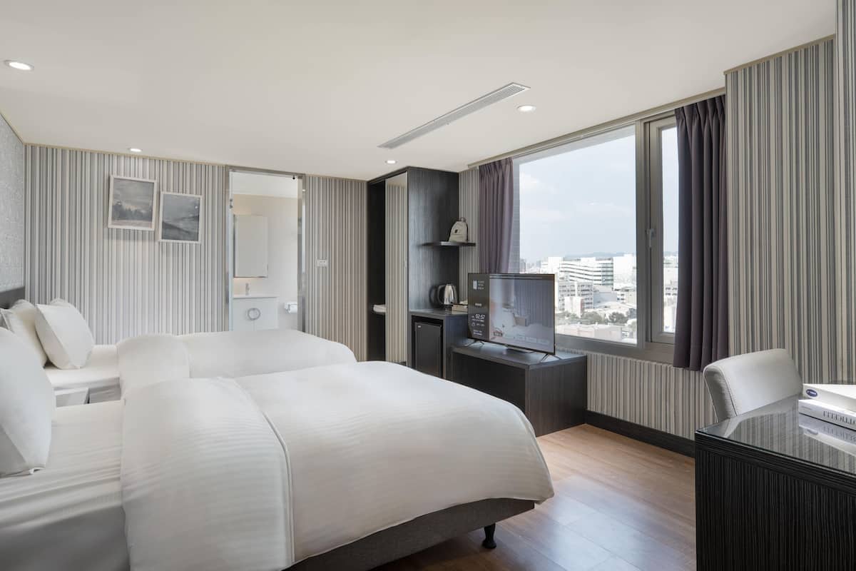 A modern hotel room with a large bed, a desk with a computer, a TV, and a city view.
