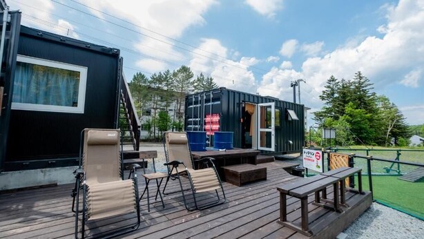 A deck with outdoor seating and a small stage, surrounded by a fenced area and trees. - C HOTEL -Biei Shirogane Pet Allowed (Biei)