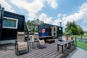 A deck with outdoor seating and a small stage, surrounded by a fenced area and trees. - C HOTEL -Biei Shirogane Pet Allowed (Biei)