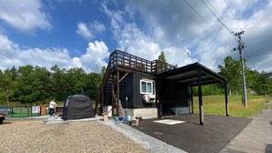 A building with a covered outdoor area, a small window, and a gravel ground. - C HOTEL -Biei Shirogane Pet Allowed (Biei)