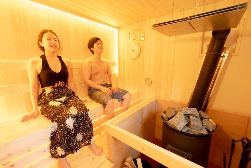 Una sala de sauna con paredes y bancos de madera. Se observa un calentador y un reloj en la pared.
