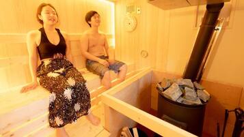Una sala de sauna con paredes y bancos de madera. Se observa un calentador y un reloj en la pared.