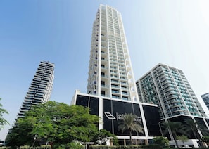Ein Hochhaus mit mehreren Balkonen, umgeben von viel Grün und weiteren modernen Gebäuden.