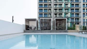 A swimming pool with lounge chairs and a modern building with balconies in the background.