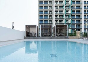 Une piscine avec des chaises longues et un bâtiment moderne doté de balcons en arrière-plan.
