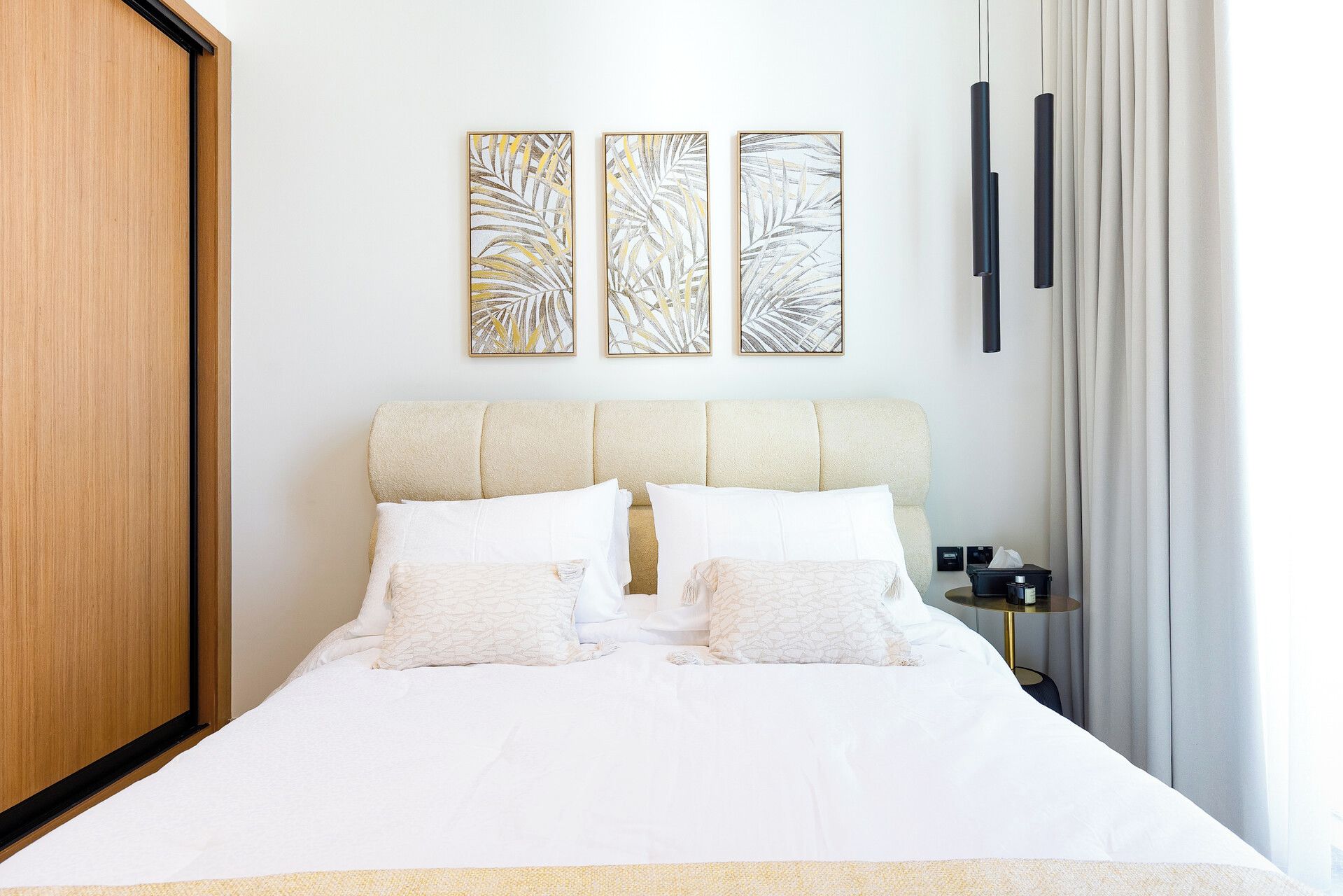 A neatly made bed with white bedding, a headboard, and two wall-mounted artworks.