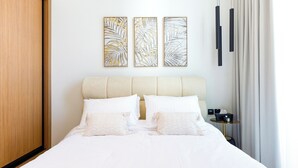 A neatly made bed with white bedding, a headboard, and two wall-mounted artworks. - Bloomfields Cozy 1Br Binghatti House  (Dubai)