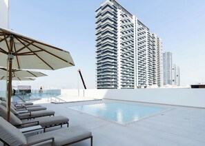 Un espace piscine aménagé sur le toit, avec des chaises longues et une vue sur les gratte-ciel.