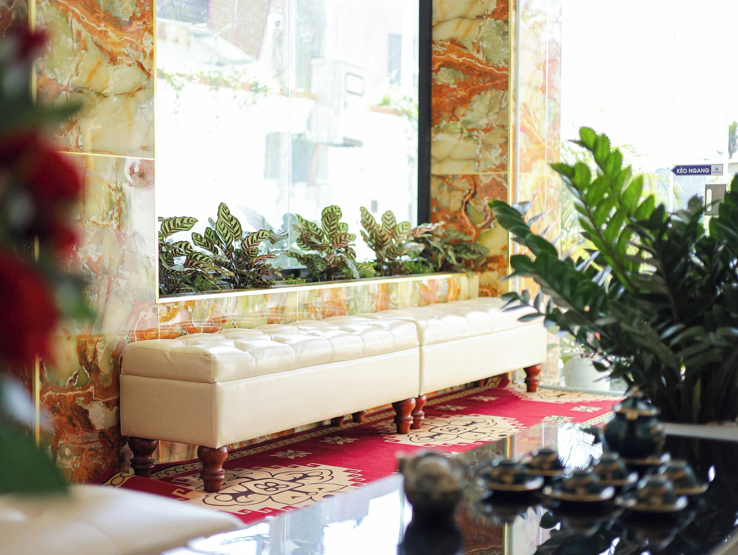 Un sofá elegante con un tapete rojo estampado, una pared de mármol y una ventana con plantas.
