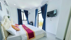 A hotel room with a large bed, a TV mounted on the wall, and a balcony with blue curtains. - Sea View Hotel Phan Thiet (Tien Thanh)