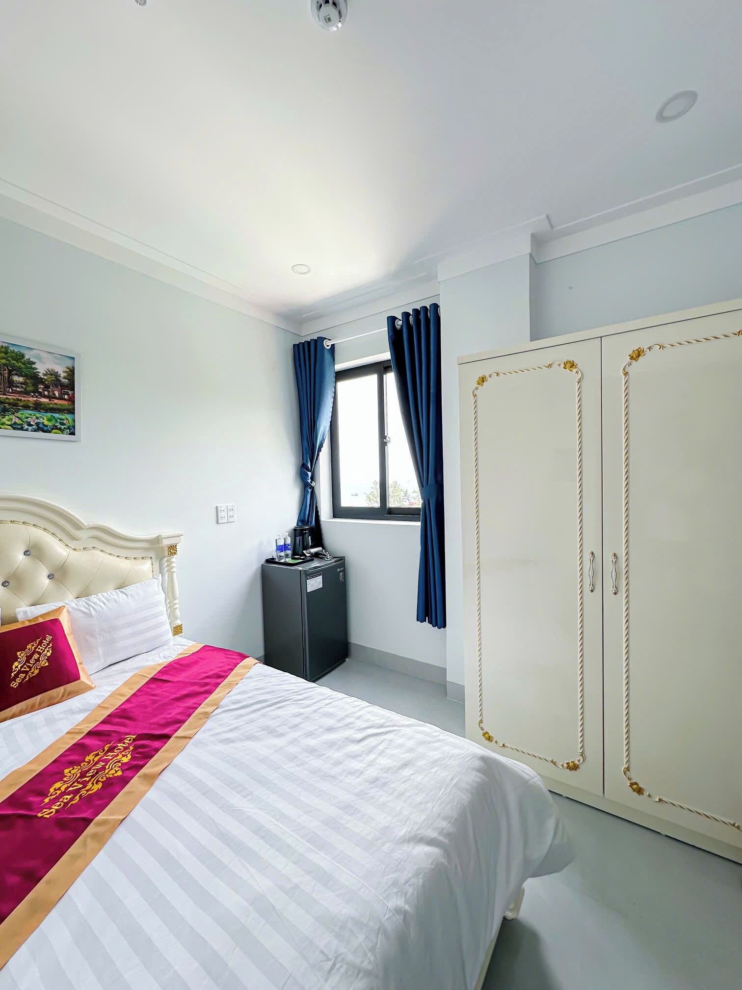 A hotel room with a bed, a wardrobe, a desk with a lamp, and a window with curtains.