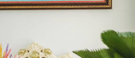 A luxurious beige sofa with ornate gold detailing and floral cushions, set against a white wall with a framed landscape painting above.