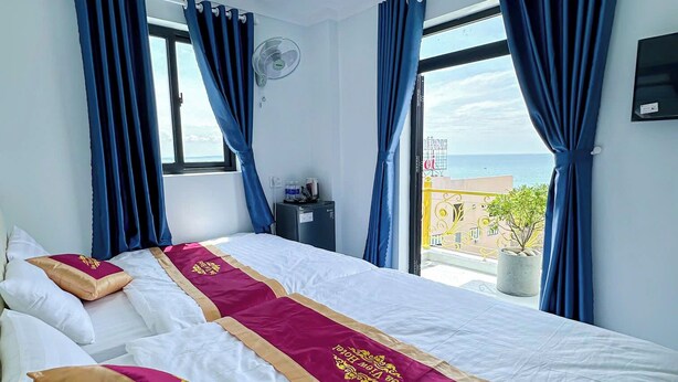 A hotel room with two beds, a large window with curtains, a ceiling fan, and a view of the sea. - Sea View Hotel Phan Thiet (Tien Thanh)
