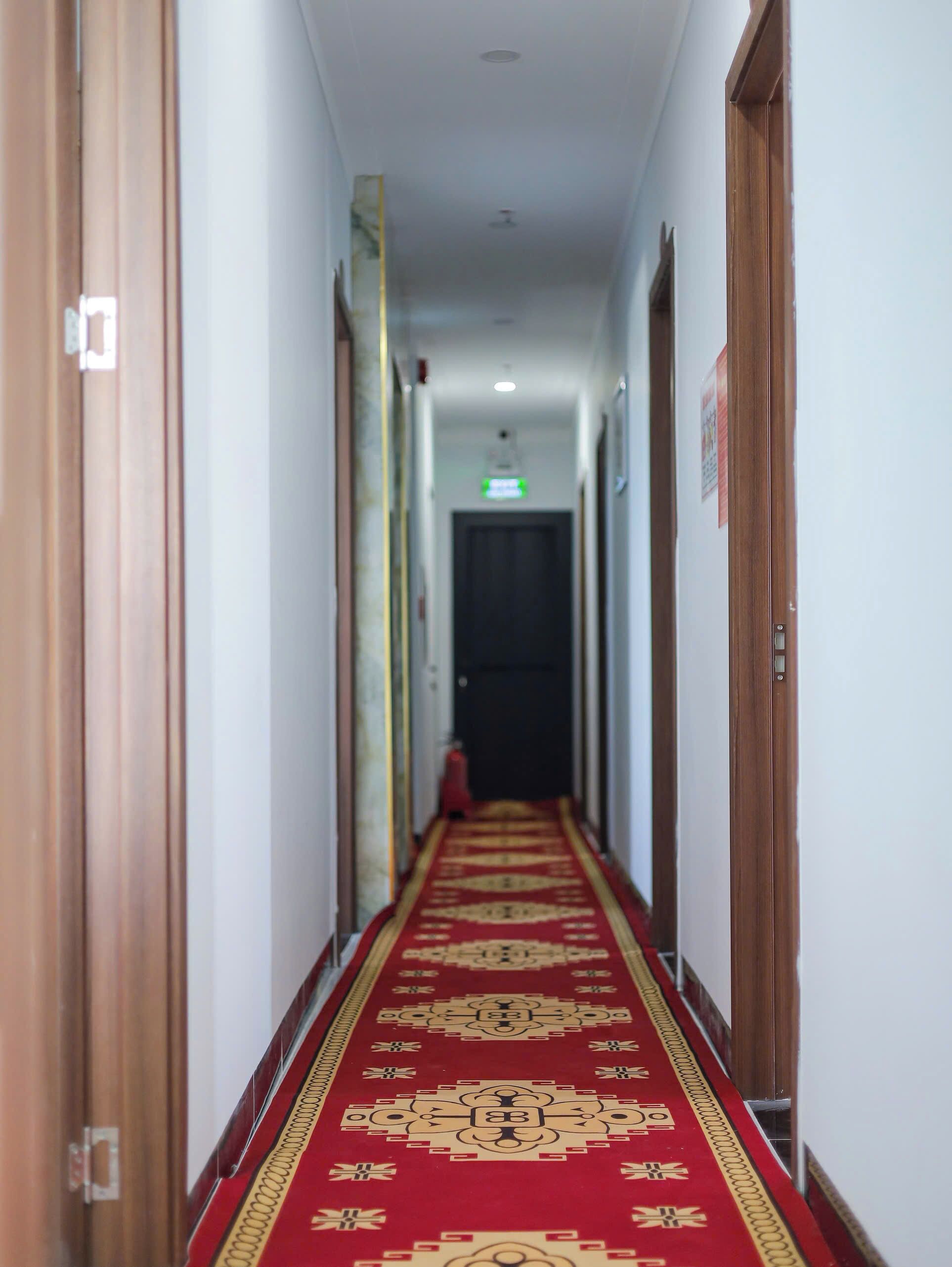 Un couloir avec un tapis rouge, des portes en bois et une porte de couleur sombre au fond.