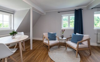 Una habitación moderna con techo inclinado, piso de madera, una mesa redonda con sillas y dos sofás con cojines estampados.