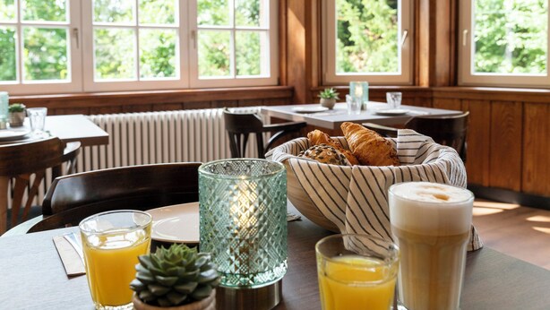 A breakfast setting with a table, a basket of croissants, glasses of orange juice, and a candle. - Wohnpark Hotel (Heppenheim)