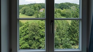 A window with a view of a green landscape and a house in the distance. - Wohnpark Hotel (Heppenheim)